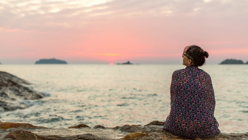 Lonely woman sitting on the seashore after sundown.